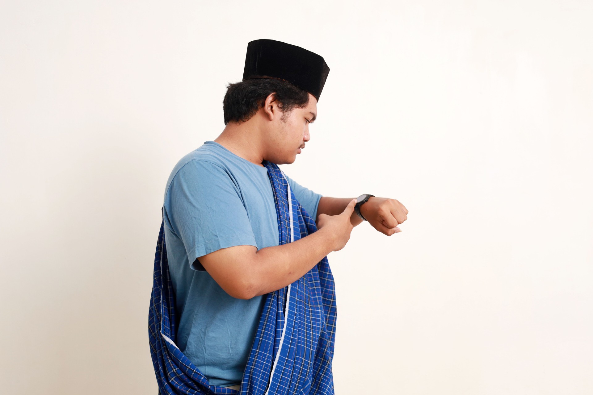 Side view of asian muslim boy standing while checking his wrist watch seriously